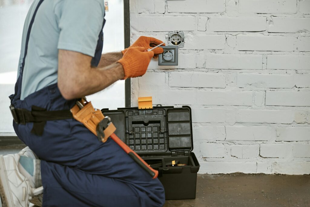 Electrician repairing power electric socket with screwdriver